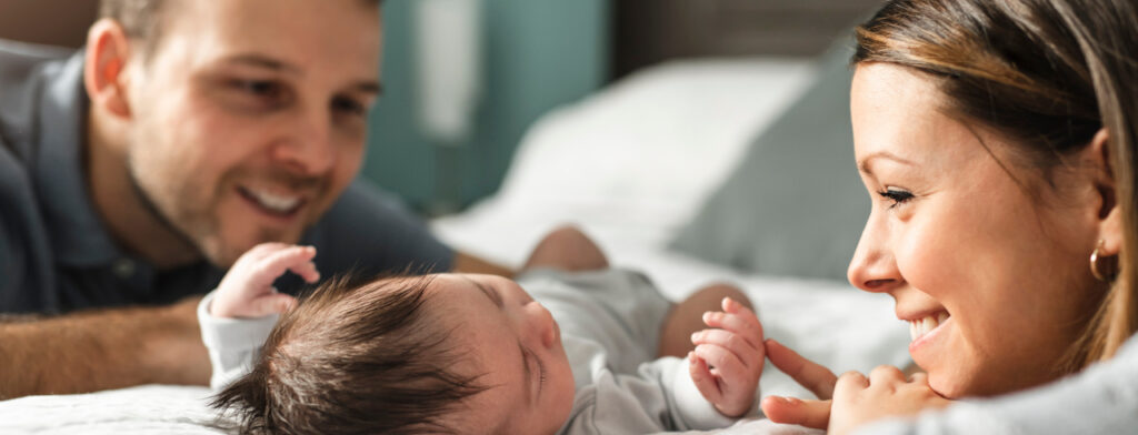 Bild von einem schönen jungen Elternpaar mit einem neugeborenem Baby im Bett.